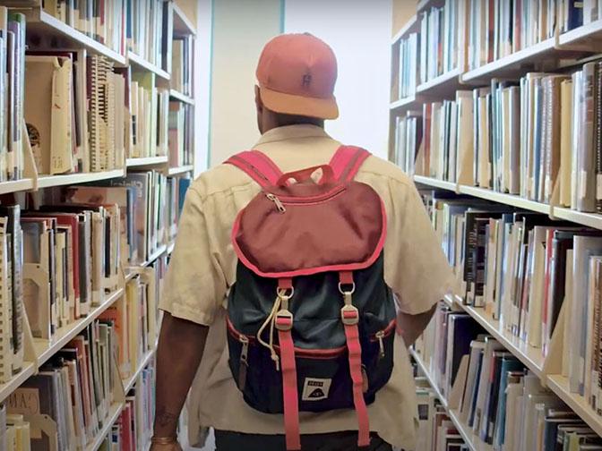 SPU alum Omni Lott walks down a row of books in the Ames Library